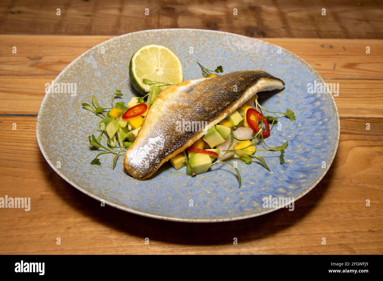Un delizioso piatto di pesce spigola con Mango e. Avocado salsa su un  tavolo da cucina in legno Foto stock - Alamy