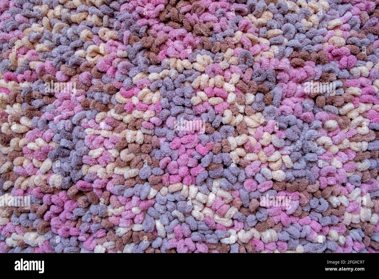 La superficie di un tappeto multicolore lavorato a maglia da un filo di lana denso e soffice, che è una serie di anelli arrotondati di colori marrone, rosa, viola e beige. R Foto Stock