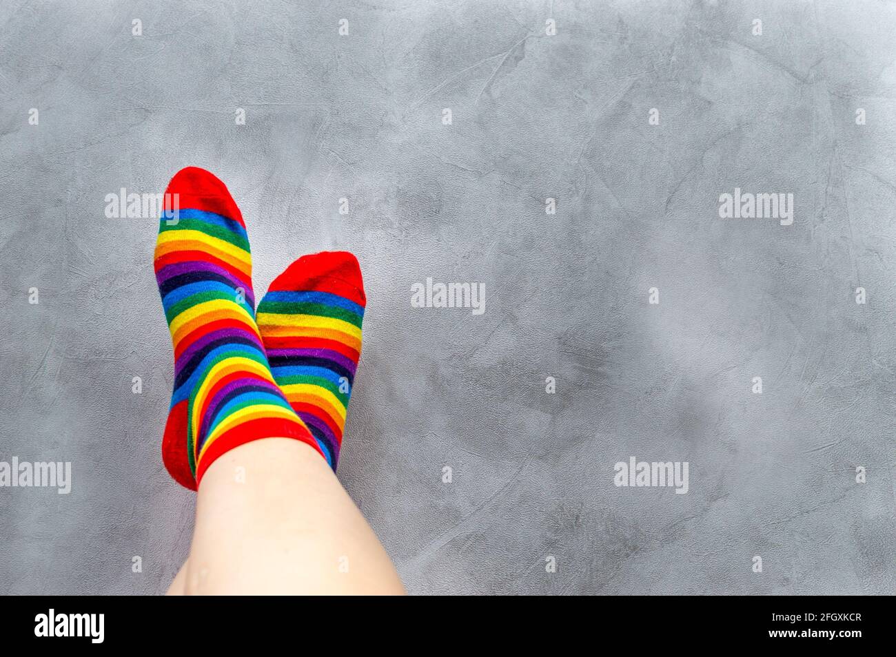 Su sfondo grigio, primo piano dei piedi di un uomo in calze multicolore. Arcobaleno. Simbolo. LGBT Concept Foto Stock