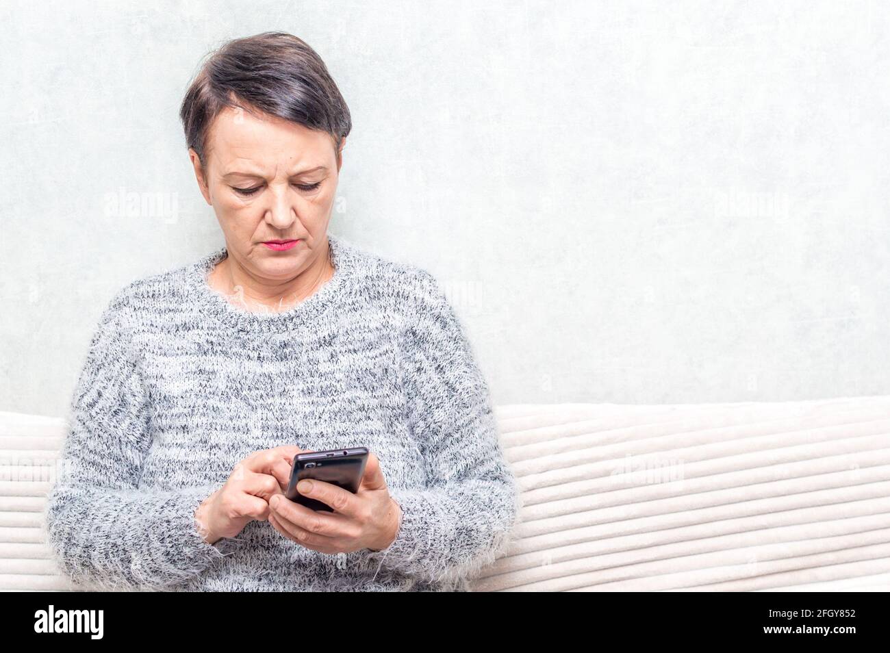 Ritratto di donna anziana ussing smartphone mentre si siede su ofa Foto Stock