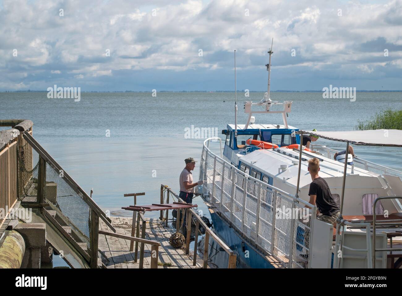 Quattro persone dipingono e mettono in ordine una piccola barca bianca da diporto, in piedi al molo sulla baia del mare sullo sfondo di orizzonte blu. Foto Stock