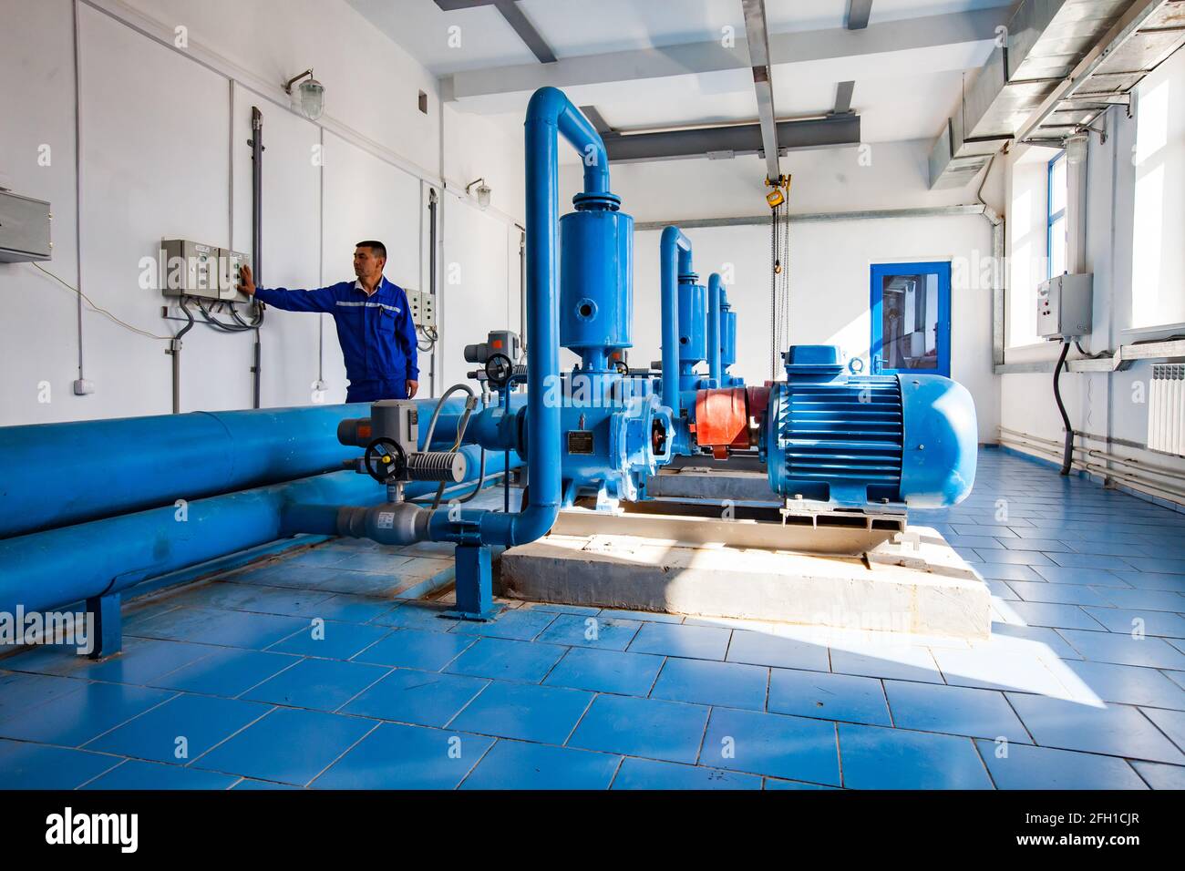 Stazione di purificazione dell'acqua, fiume Shardara. Pompe di acqua di controllo del lavoratore asiatico. Pavimento in piastrelle industriali blu. Kyzylorda, Kazakistan. Foto Stock