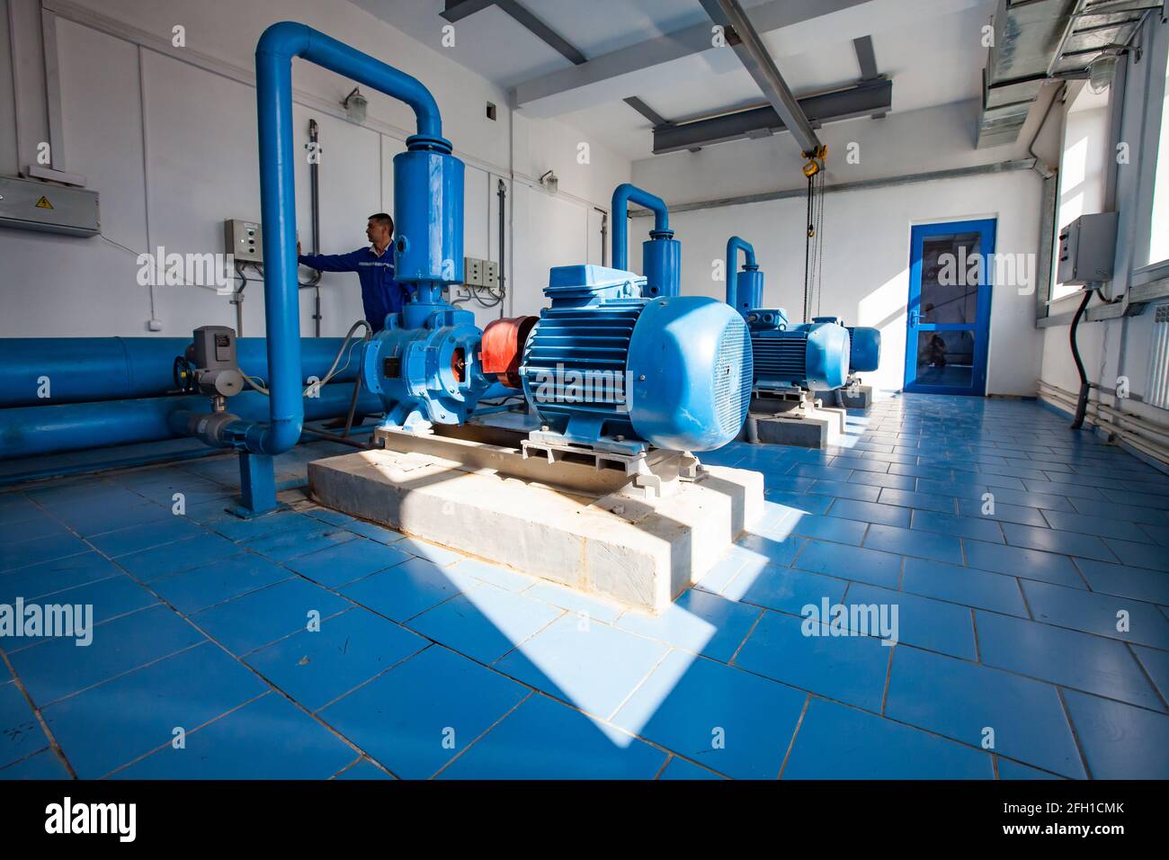 Kyzylorda, Kazakhstan: Stazione di depurazione dell'acqua sul fiume Shardara. Pompe di acqua di controllo del lavoratore asiatico. Pavimento in piastrelle industriali blu. Foto Stock