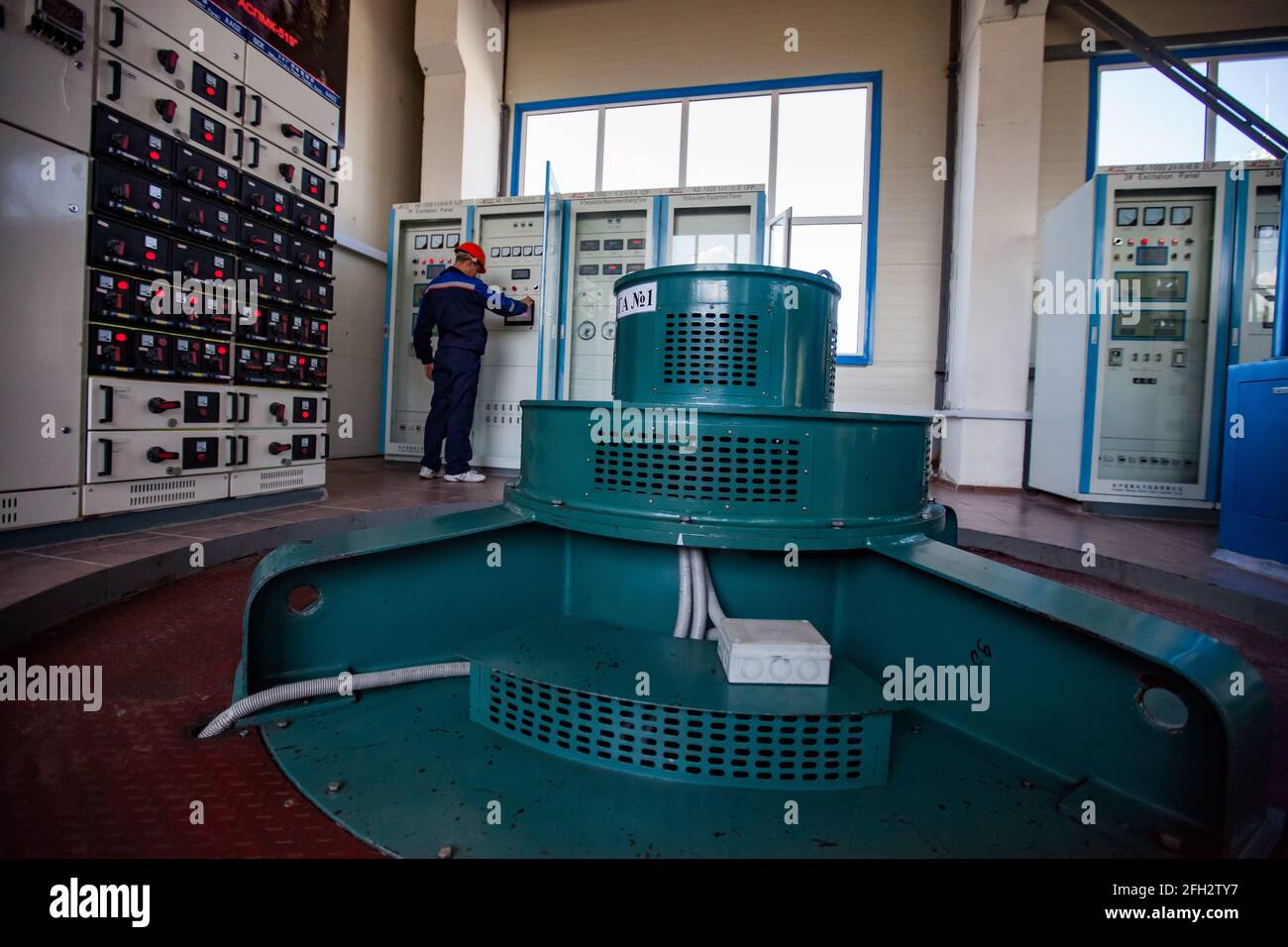 Sala macchine per centrali idroelettriche. Generatori elettrici verdi. Pannelli di controllo, indicatori, commutatori. Il lavoratore controlla gli armadi elettrici di alimentazione Foto Stock