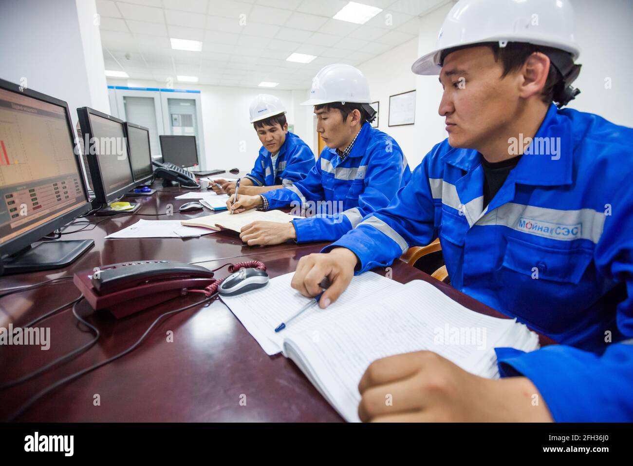 Centrale idroelettrica Moinak, sala di controllo. Tre operatori asiatici che sovrintende ai processi. L'uomo destro offuscato, l'uomo centrale a fuoco. Foto Stock