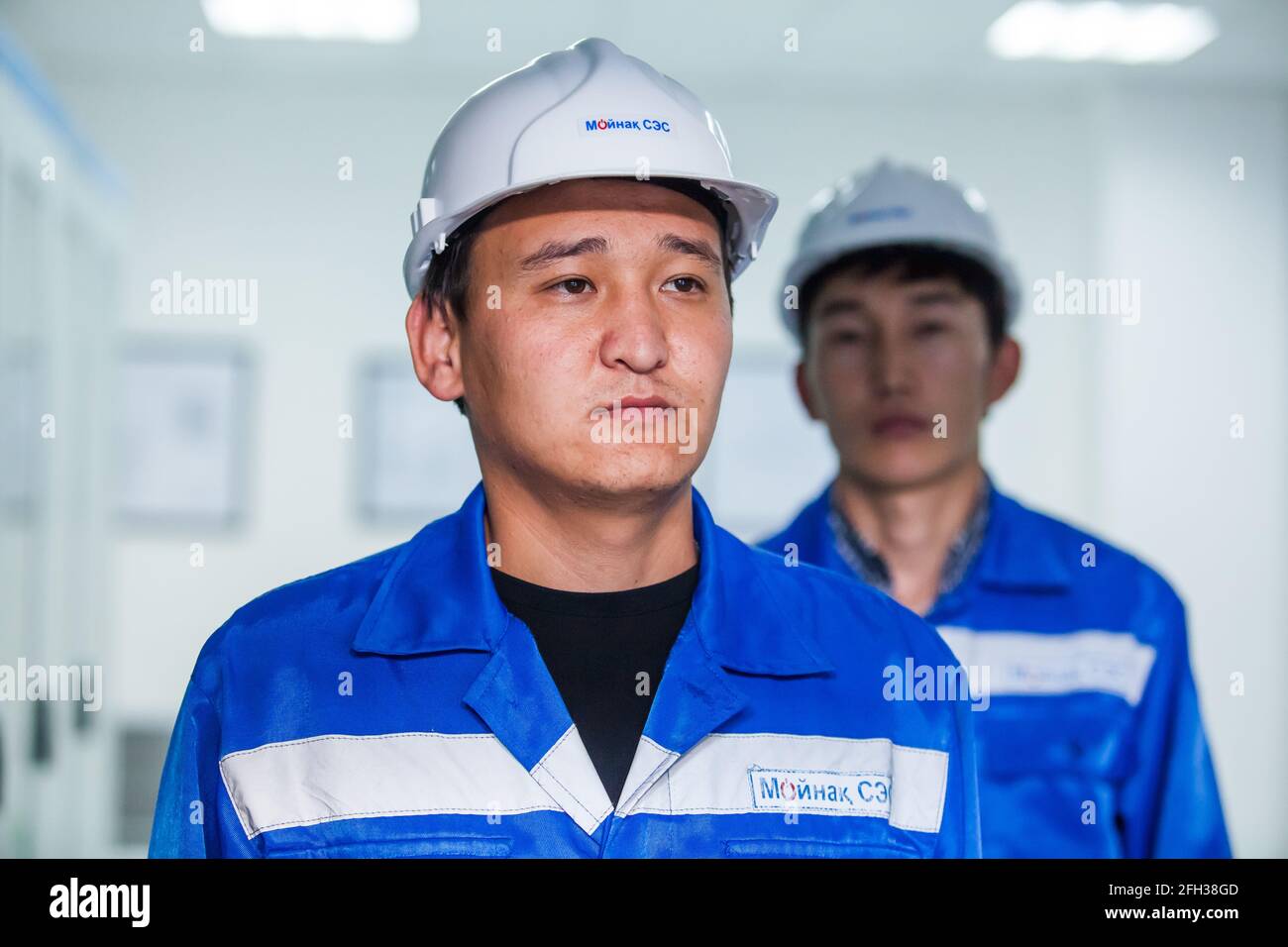 Centrale idroelettrica Moinak. Due giovani operatori asiatici in posa. A sinistra a fuoco, a destra sfocata in ombra. Copricapi bianche, abbigliamento da lavoro blu. Foto Stock