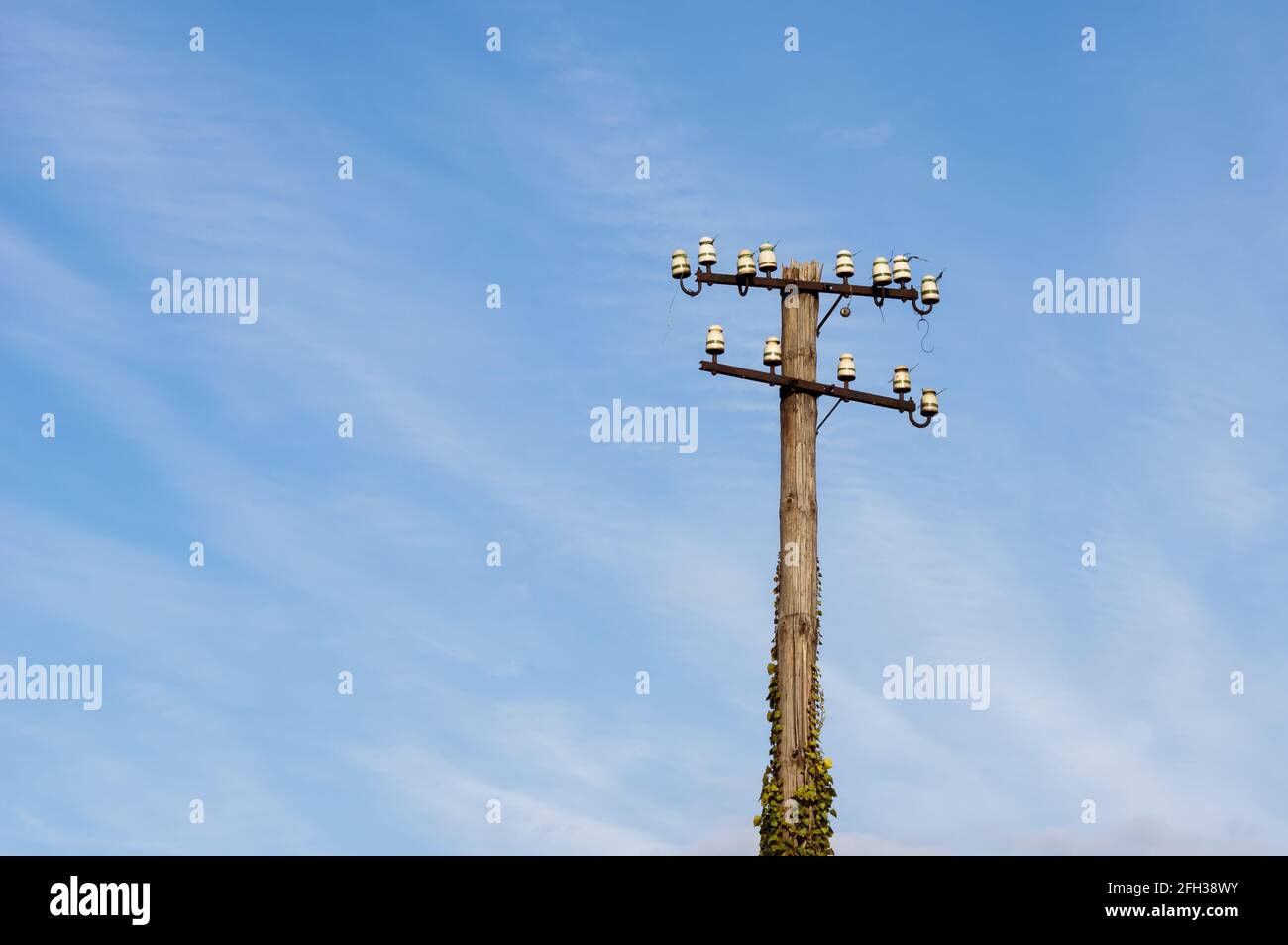 Vista ad angolo basso del vecchio e decadente palo di telegrafia in una stazione ferroviaria in Germania contro cielo blu con le nuvole di cirrus. Messa a fuoco selettiva in primo piano. Foto Stock