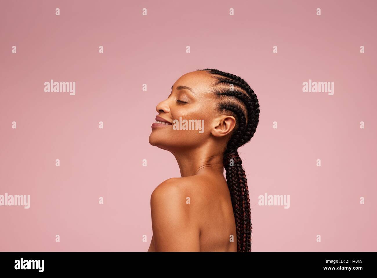 Vista laterale di un modello femminile con pelle sana e impeccabile. Donna afroamericana con acconciatura intrecciata su sfondo rosa. Foto Stock