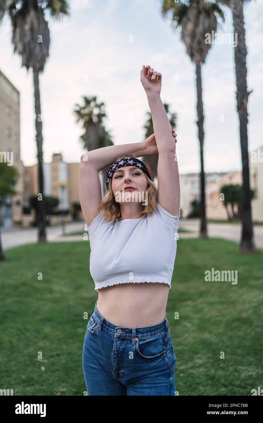 Contenuto americano femmina in piedi bandana con le braccia sollevate prato con palme in città e vista lontano Foto Stock