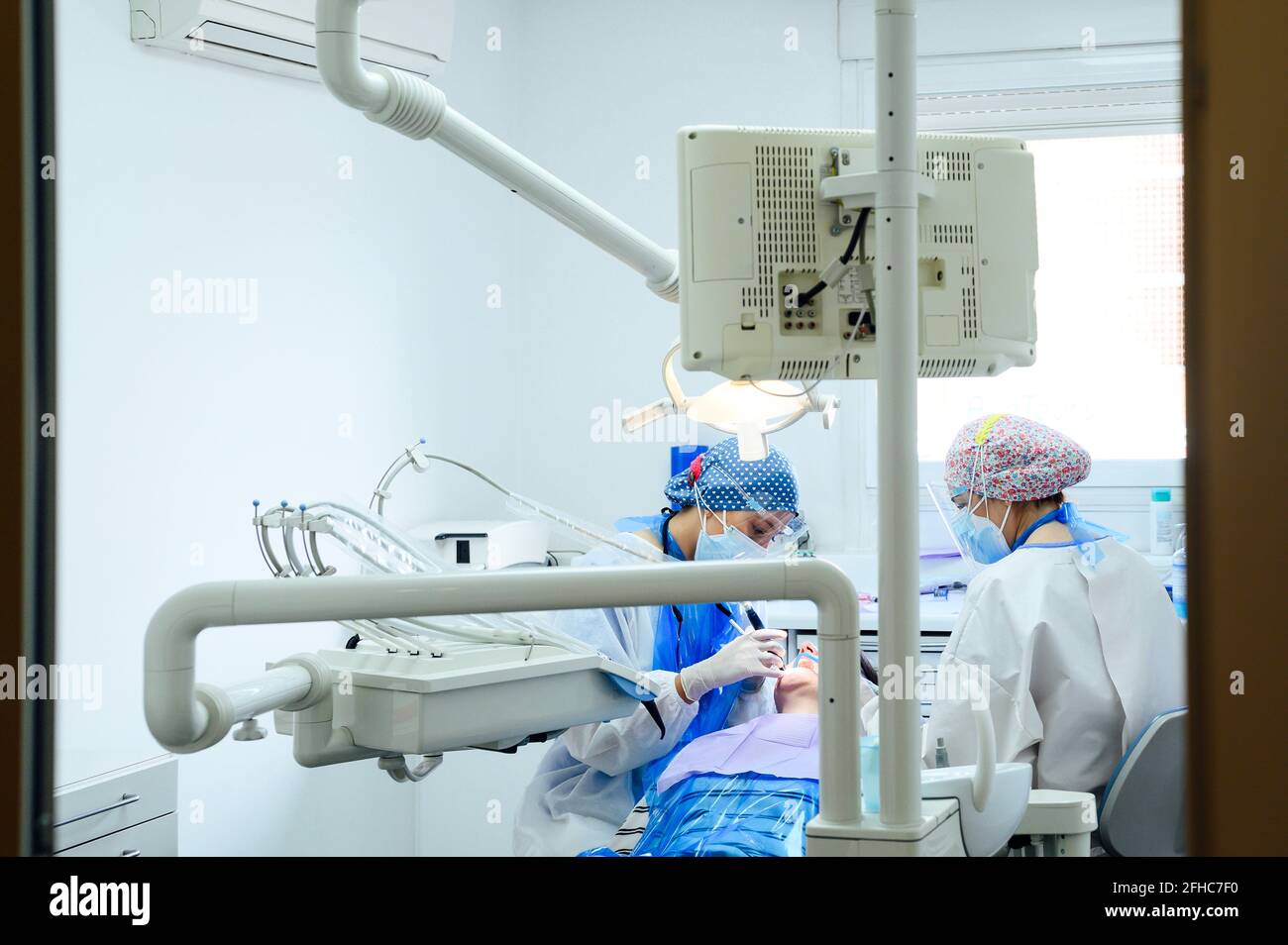 Dentista anonimo con un collega in uniformi denti operativi del paziente utilizzo di strumenti medici in clinica moderna Foto Stock