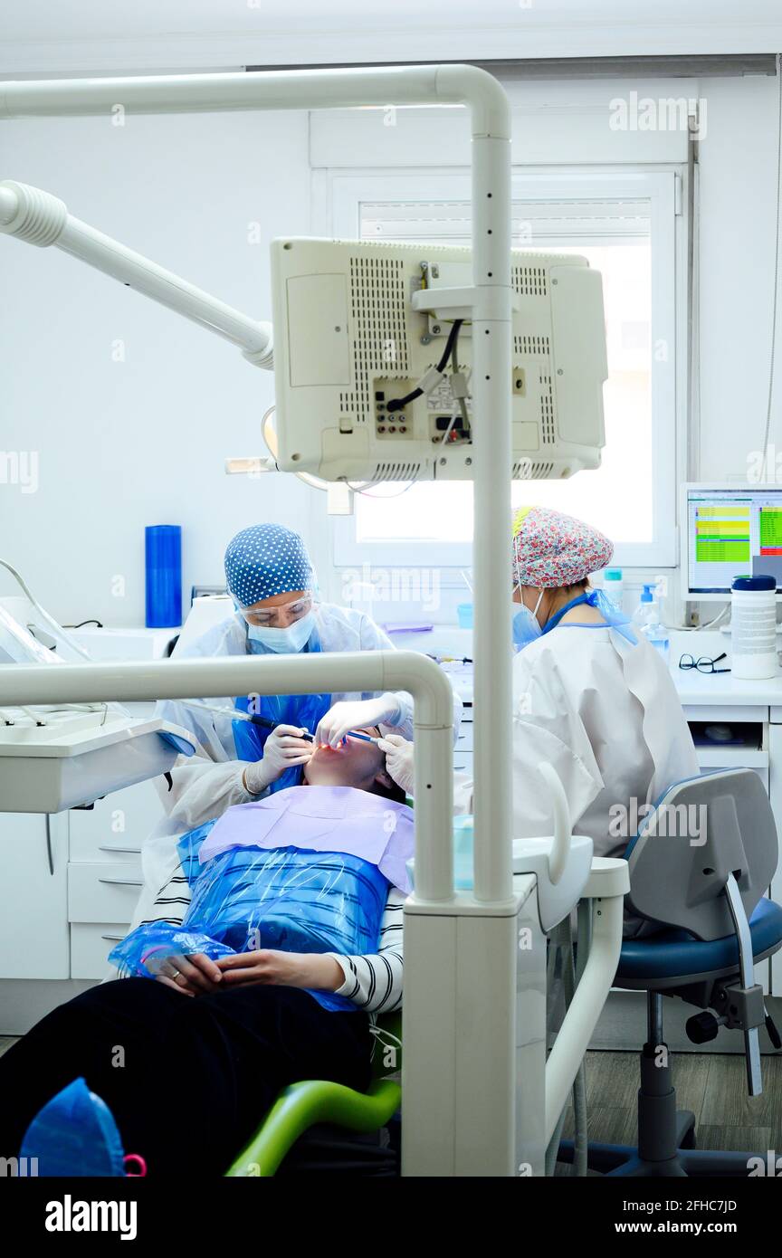 Dentista anonimo con un collega in uniformi denti operativi del paziente utilizzo di strumenti medici in clinica moderna Foto Stock