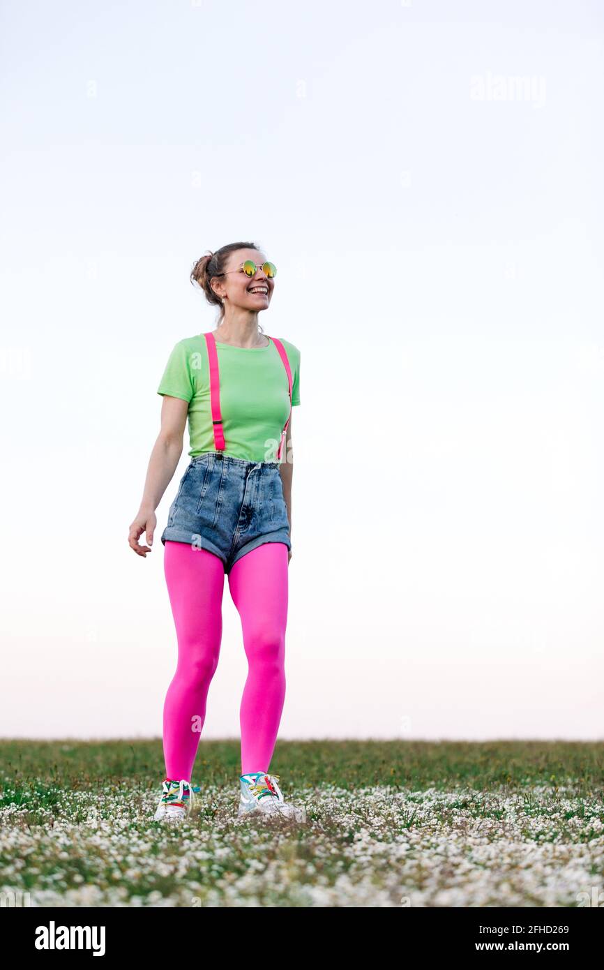 Calzoncini corti e rosa brillante per una giovane donna dal corpo pieno calze che camminano merrily su glade erbosa lussureggiante nella natura Foto Stock