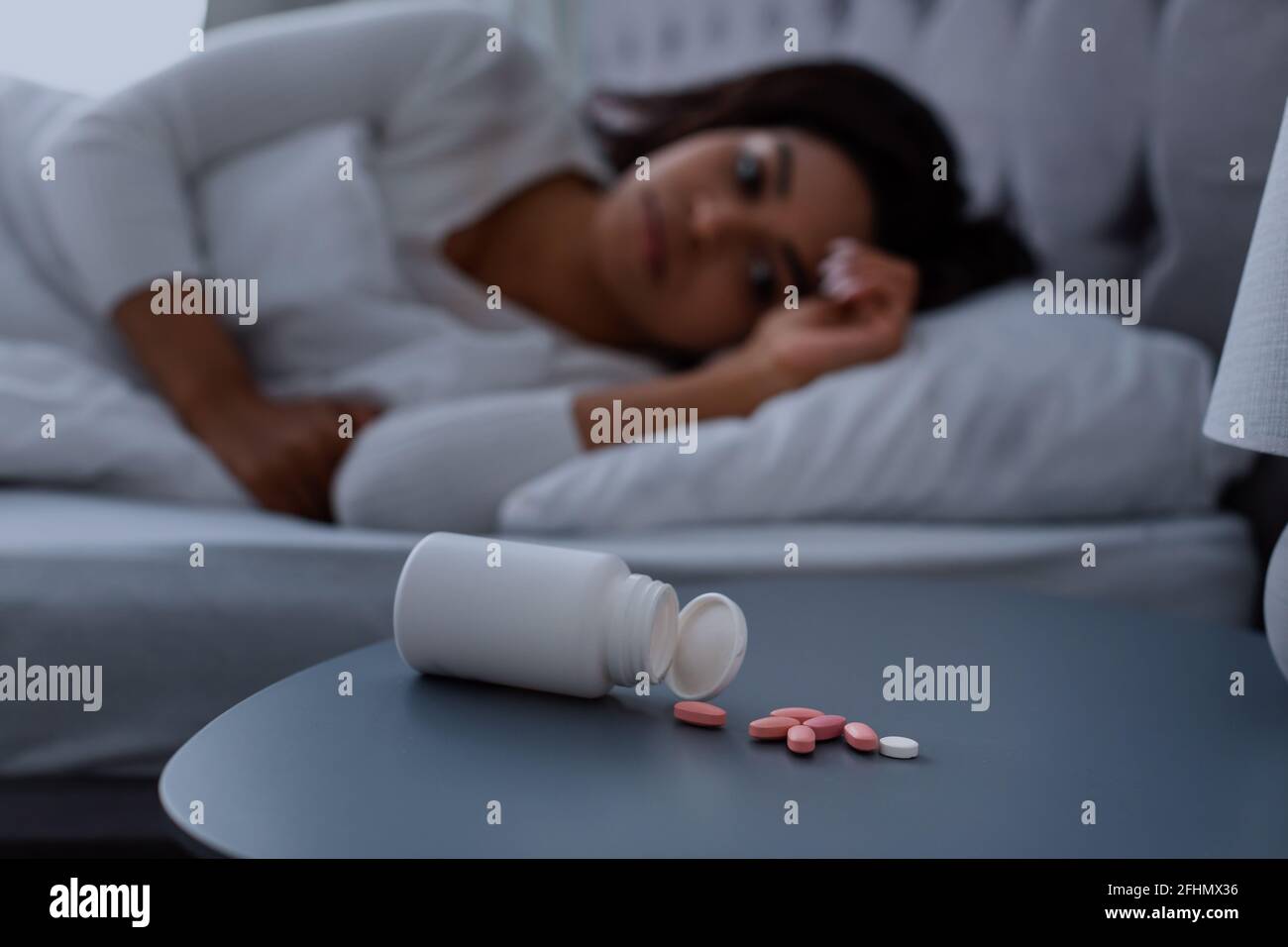 Donna nera che soffre di insonnia, pillole che giacciono sul tavolo Foto Stock