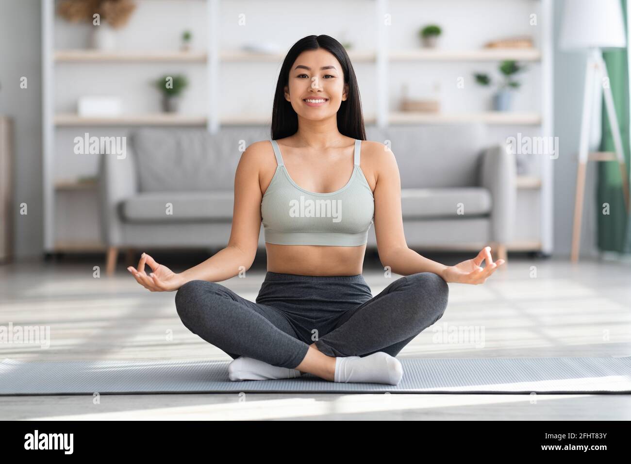 Yoga domestico. Felice giovane donna asiatica meditando a casa in lotus posizione Foto Stock