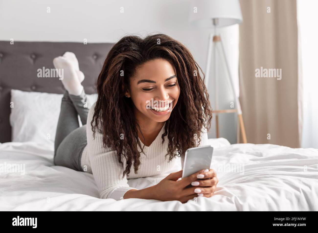 Donna nera felice che si trova a letto leggendo un messaggio di testo Foto Stock