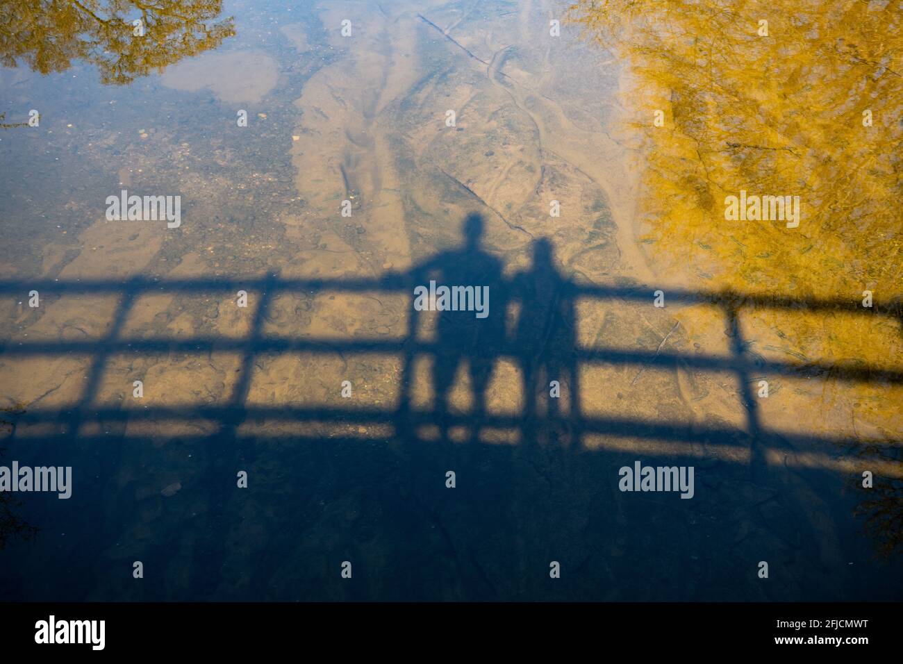 Ombre di due figure su un ponte nel fiume con riflessi di alberi - Scozia, Regno Unito Foto Stock
