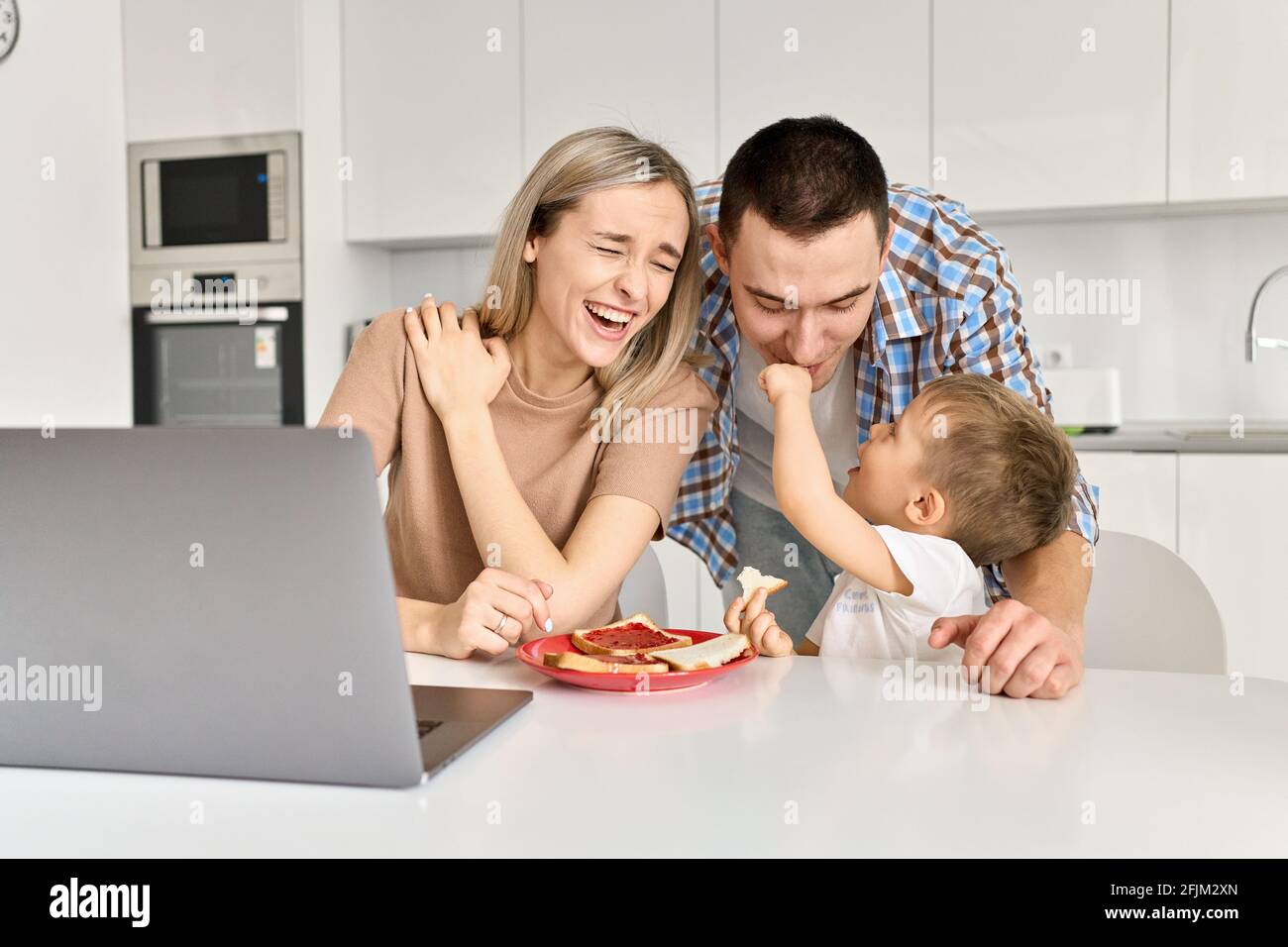 Felice giovane famiglia con figlio di capretto che si diverte a mangiare toast in cucina. Foto Stock