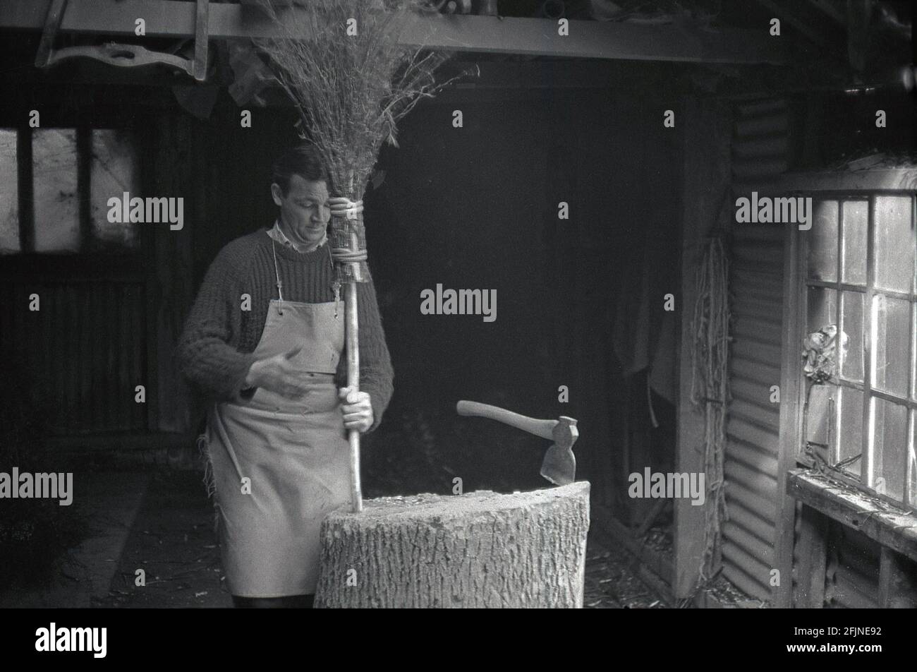 Anni '50, storico, un artigiano maschile nel suo laboratorio di fare una scopa, Inghilterra, Regno Unito. Un'antica imbarcazione, la realizzazione di scopa, conosciuta anche come 'besoms' o 'besom making', consiste in un fascio di ramoscelli di alberi legati saldamente intorno ad un bastone. Tradizionalmente, le scope besom erano fatte da ramoscelli dell'albero della betulla e uno squire della scopa del villaggio ed entrambi i coppiceworker li hanno prodotti. Oggi, come molti antichi mestieri, questo mestiere altamente specializzato è quasi completamente morto fuori e ci sono ora meno di cinque creatori di besom nel Regno Unito che fanno le scopa su una base commmerica. Foto Stock