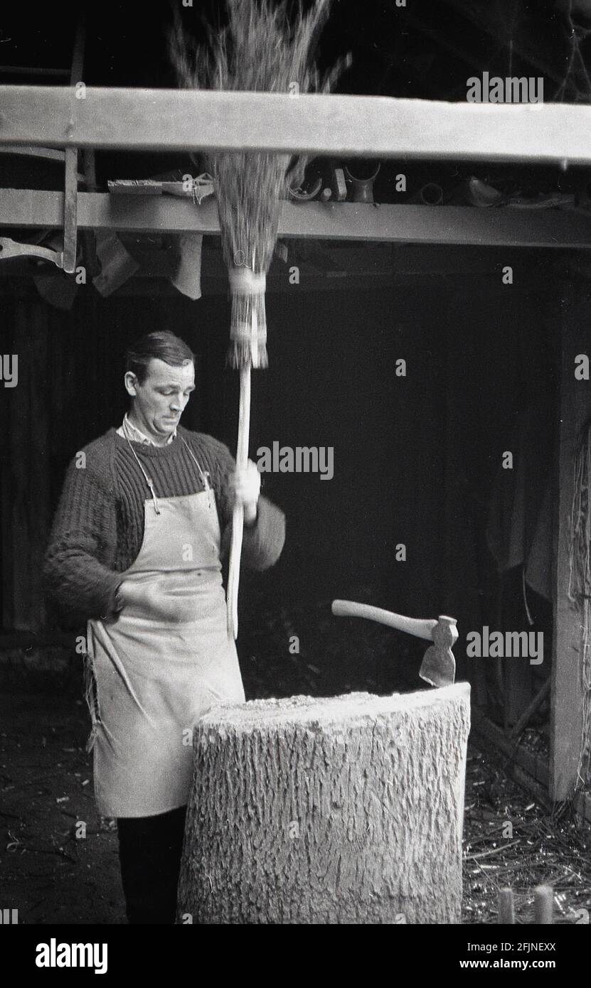 Anni '50, storico, un artigiano maschile nel suo laboratorio di fare una scopa, Inghilterra, Regno Unito. Un'antica imbarcazione, la realizzazione di scopa, conosciuta anche come 'besoms' o 'besom making', consiste in un fascio di ramoscelli di alberi legati saldamente intorno ad un bastone. Tradizionalmente, le scope besom erano fatte da ramoscelli dell'albero della betulla e uno squire della scopa del villaggio ed entrambi i coppiceworker li hanno prodotti. Oggi, come molti antichi mestieri rurali, questo commercio artigianale altamente specializzato è quasi completamente morto fuori e ci sono ora meno di cinque creatori di besom nel Regno Unito che fanno le scopa su una base commmerica. Foto Stock