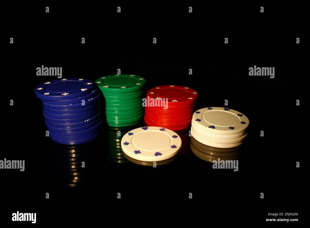 Quattro colori chip casinò stack con un chip bianco di fronte, isolato su nero con riflessione Foto Stock