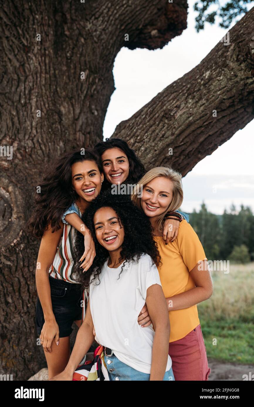 Gruppo di giovani donne diverse che si trovano di fronte a un grande albero Foto Stock