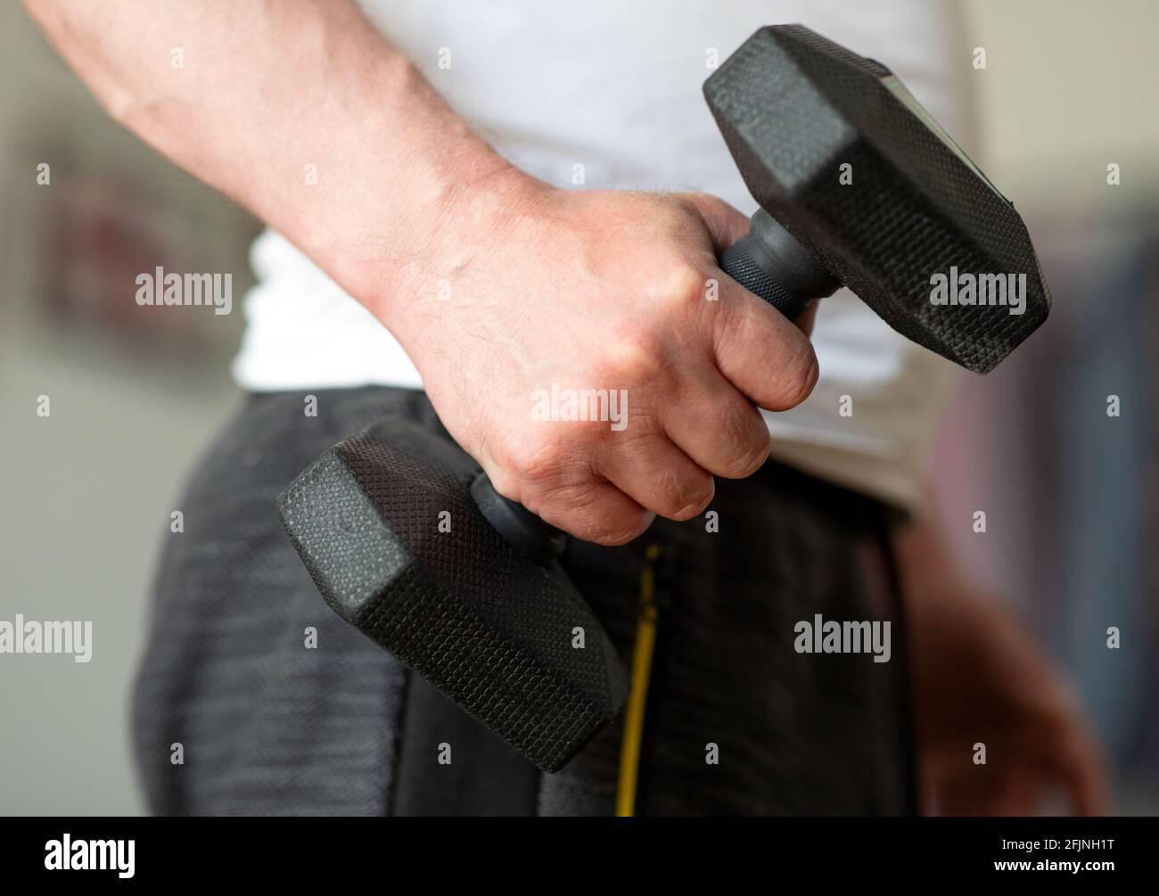Allenati con i manubri a casa. L'uomo si sta esercitando a casa. Closeup di una mano maschio con un manubri di 5 kg Foto Stock
