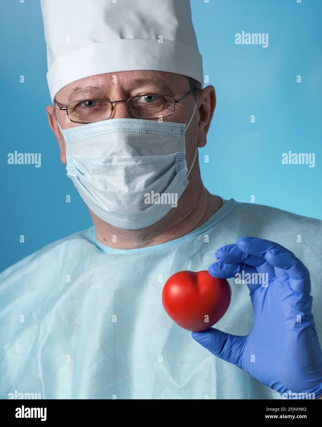 Ritratto di un cardiologo esperto di mezza età in abbigliamento medico:  Cappuccio, guanti, vestaglia e maschera, occhiali. Nelle mani di Foto stock  - Alamy