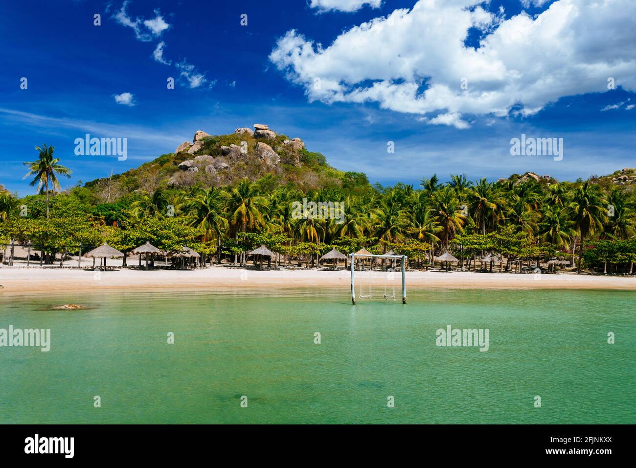 Concetto di vacanza tropicale. Una esotica spiaggia di sabbia vuota con un mare calmo e limpido, un'altalena in legno nel mare e con un bellissimo paesaggio nel backgrou Foto Stock