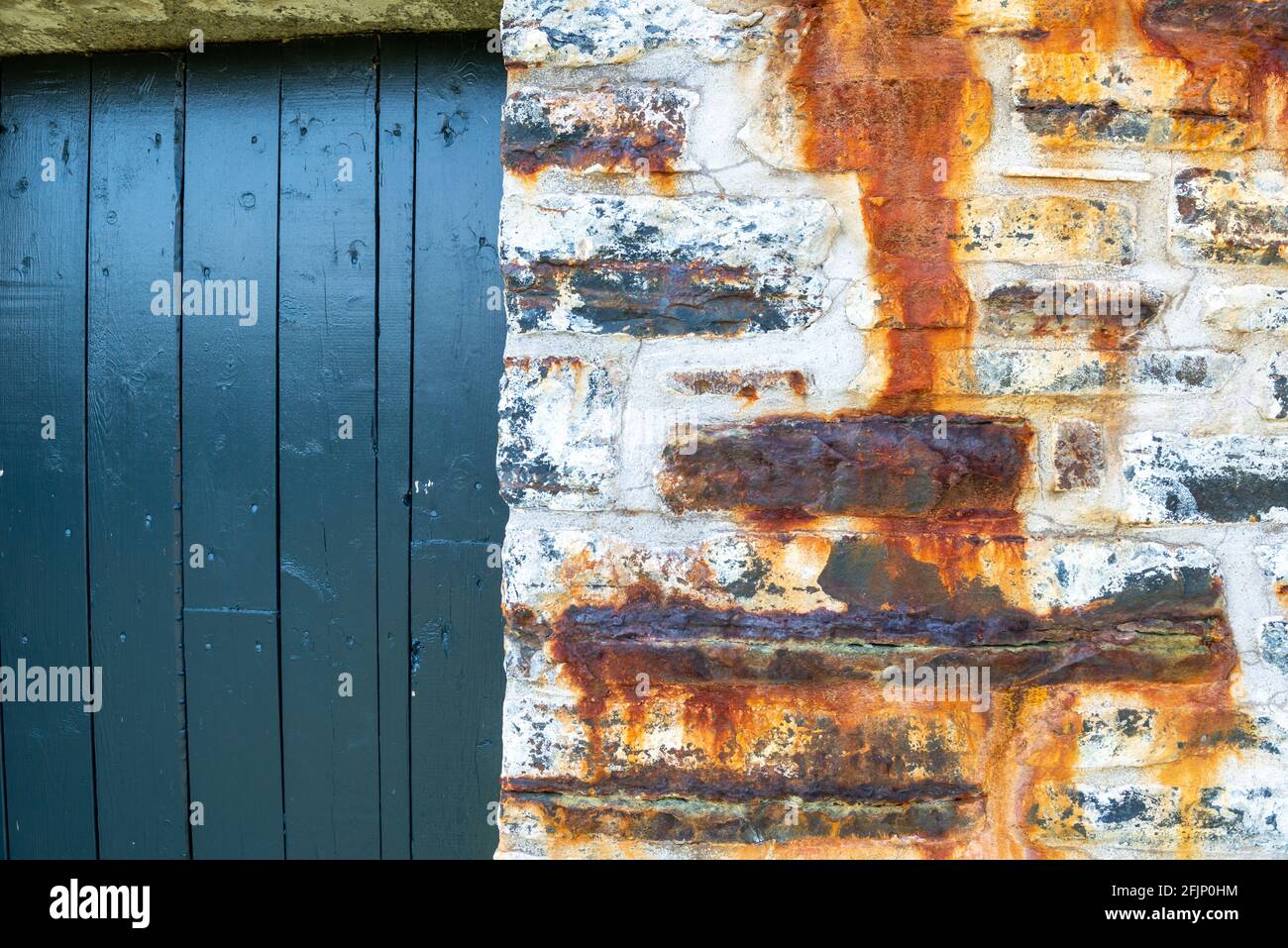 Una porta esterna in legno vintage blu luminoso con una piccola finestra che si apre sulla parte superiore. L'entrata e' in una vecchia parete di roccia rustica e testurizzata. Foto Stock