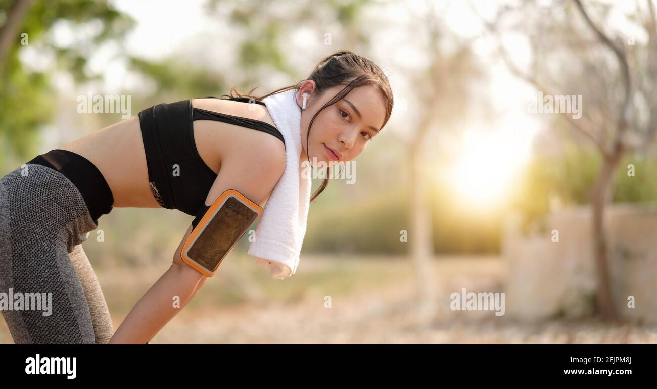 ripresa di una giovane bella atleta asiatica che riposa dopo aver fatto jogging con gli auricolari contro al parco. Foto Stock