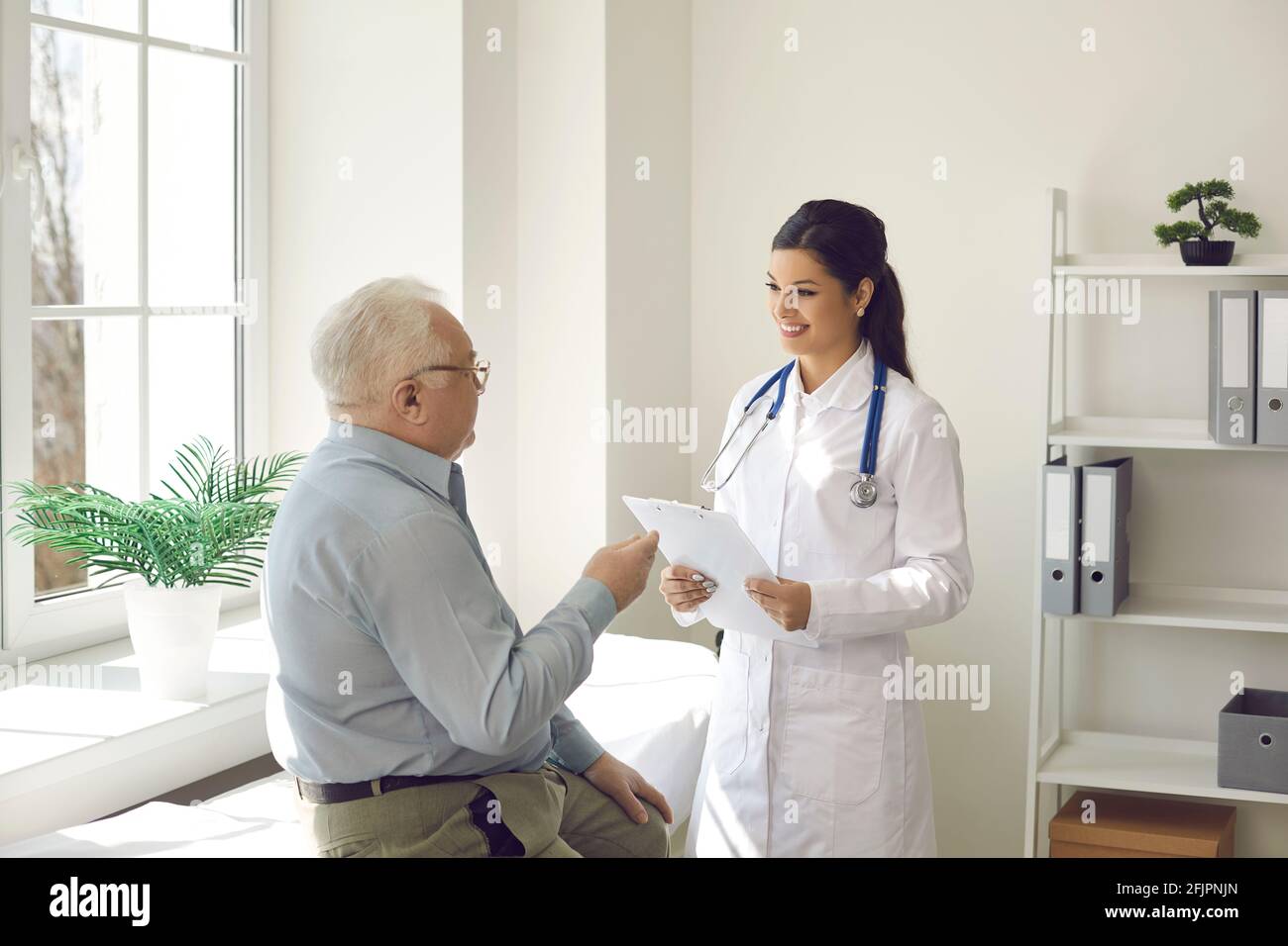 Un medico sorridente che ascolta il paziente anziano seduto all'esame letto nel suo ufficio Foto Stock