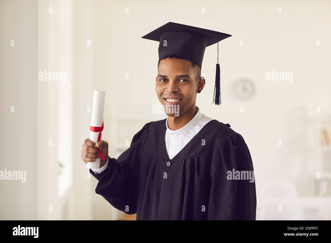 Alunno afroamericano in abito nero accademico e diploma di titolare del CAP e sorridendo Foto Stock