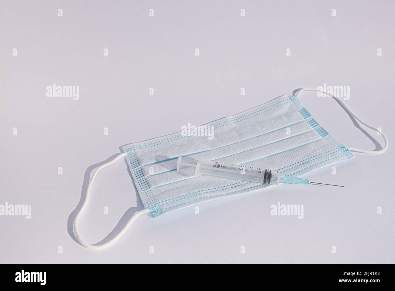 Siringa e maschera blu su sfondo bianco con spazio per la copia, Danimarca, 25 aprile 2021 Foto Stock