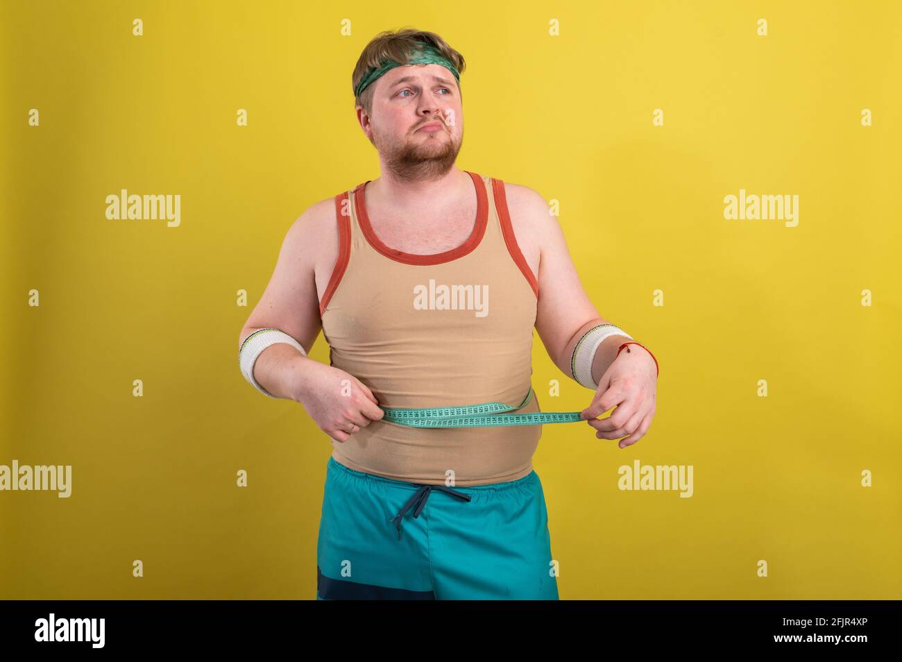 divertente uomo grasso in sportswear prende le misure del volume del corpo Foto Stock