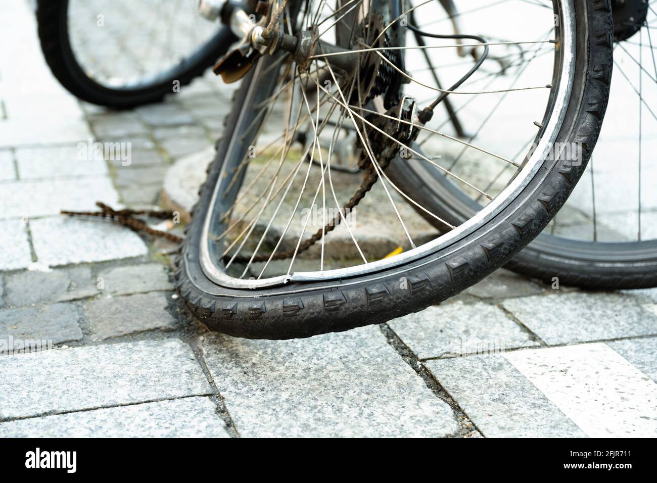 Il pneumatico posteriore piegato di una bicicletta in città con catena distrutta. Foto Stock