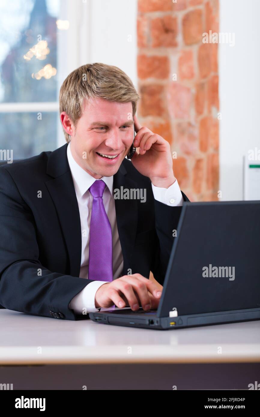 Giovane avvocato a lavorare nel suo ufficio, egli seduti alla scrivania e al telefono è un cliente o client Foto Stock
