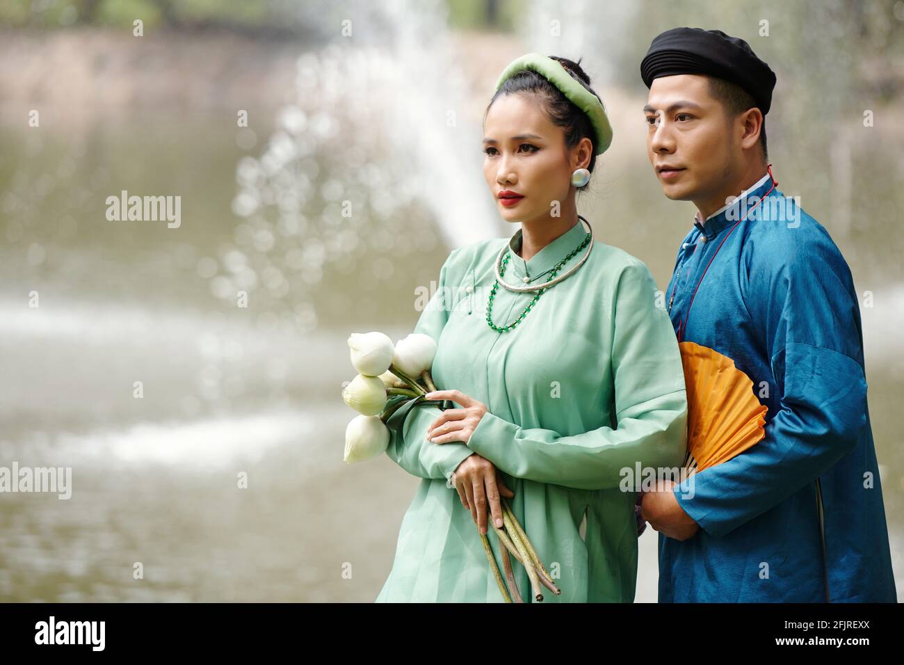 Grave bella giovane vietnamita appena sposato coppia in abiti tradizionali e copricapo in piedi all'aperto dopo il matrimonio Foto Stock