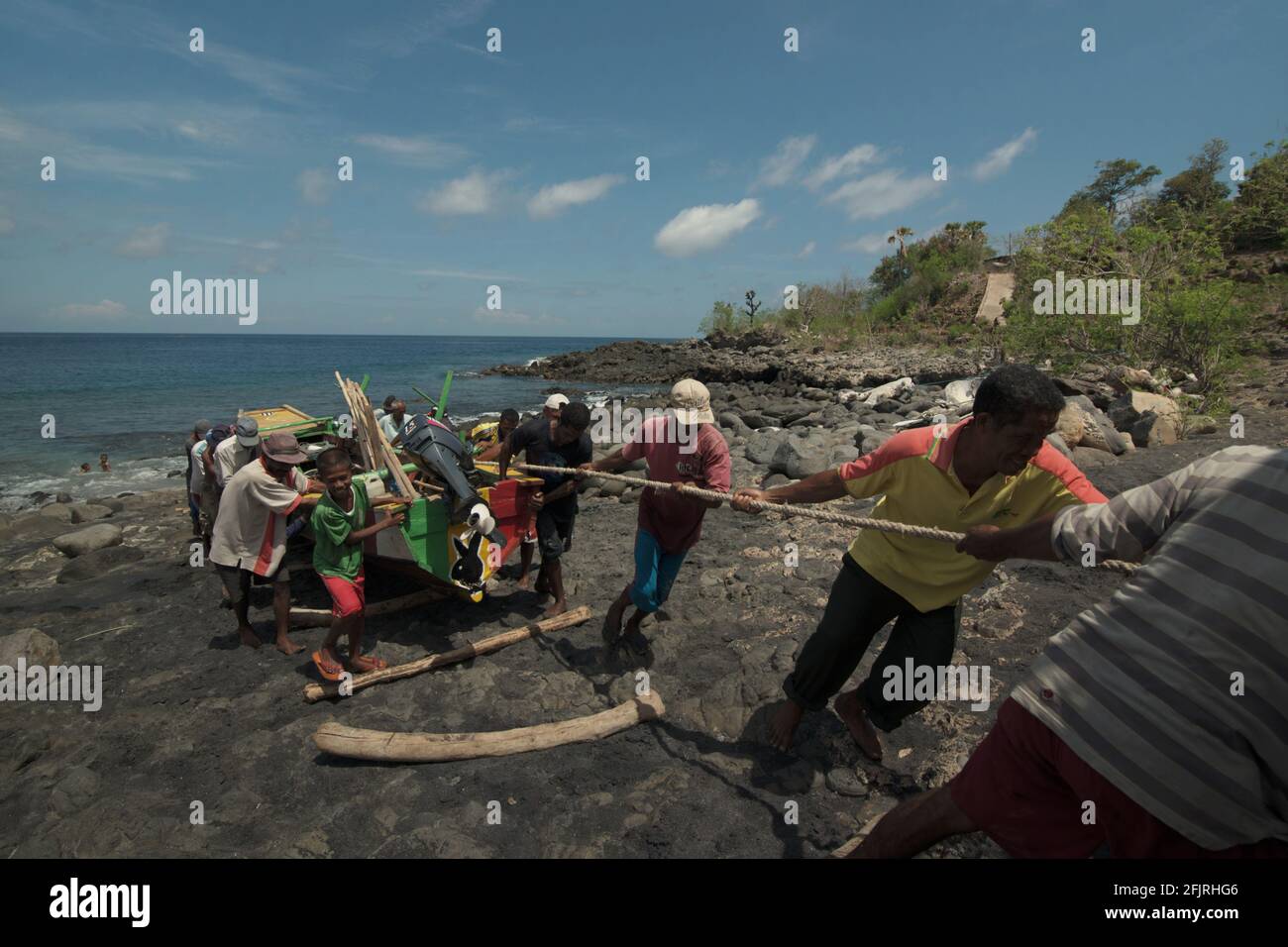 La gente che tira una barca insieme su una spiaggia rocciosa chiamata 'Lamalera B' nel villaggio di balena di Lamalera a Lembata, Nusa Tenggara orientale, Indonesia. Foto Stock