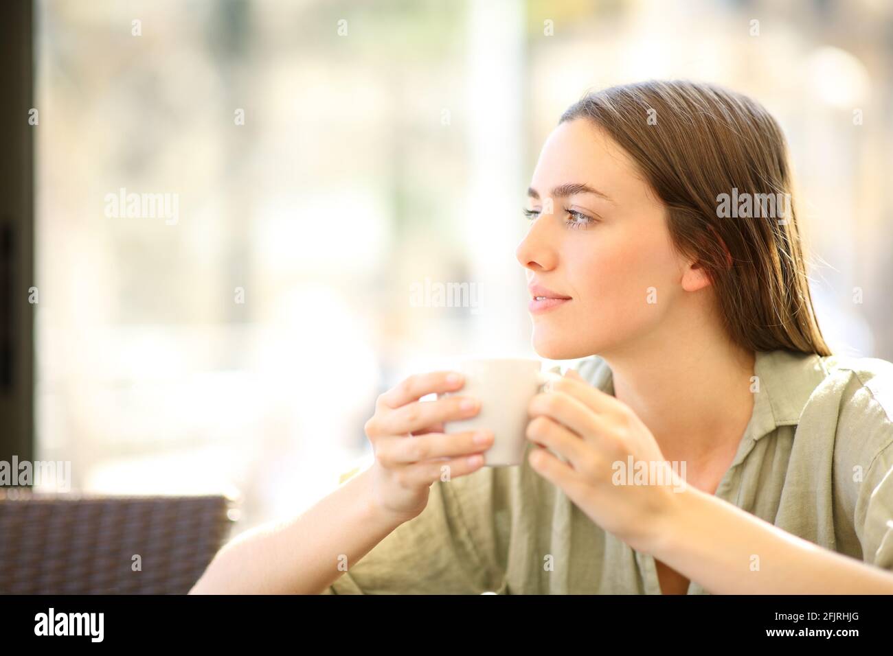 Donna rilassata che beve il caffè dalla tazza guardando il lato dentro un bar Foto Stock