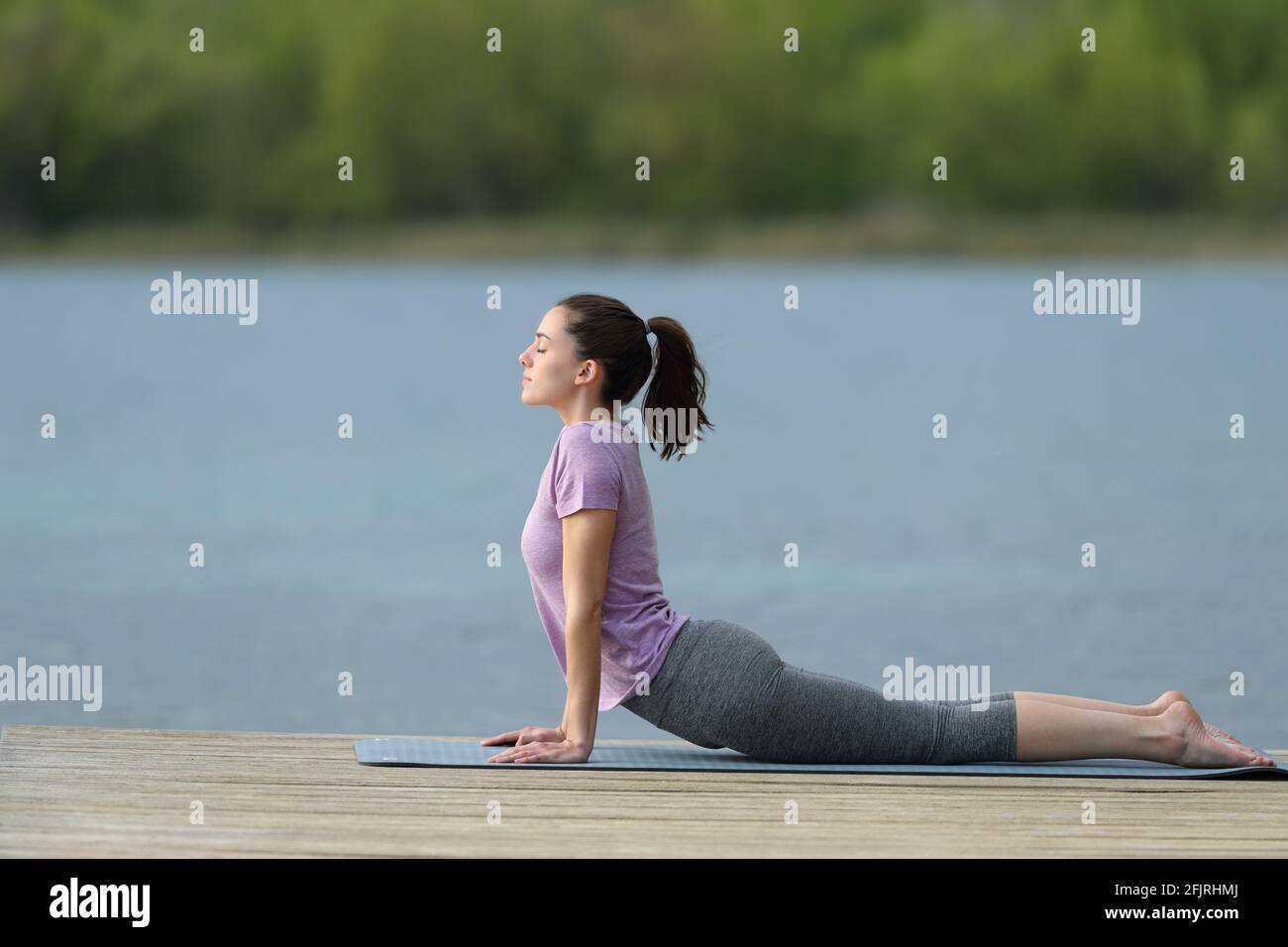 Profilo di una donna che fa yoga posa in un lago molo in estate Foto Stock