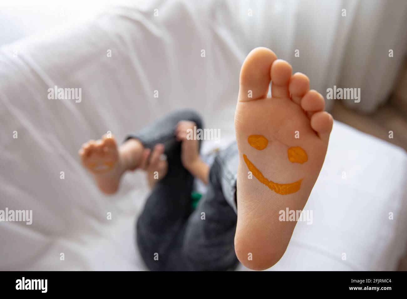 Una bambina è sdraiata su un divano con i suoi piedi dipinti con vernici. Sorrisi divertenti sui piedi dei bambini. Foto Stock