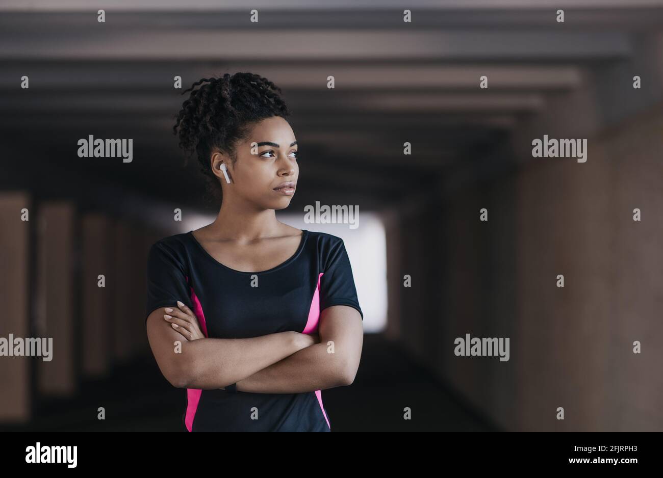 Ritratto di giovane, atletica e attraente donna afroamericana in abbigliamento sportivo e cuffie wireless Foto Stock