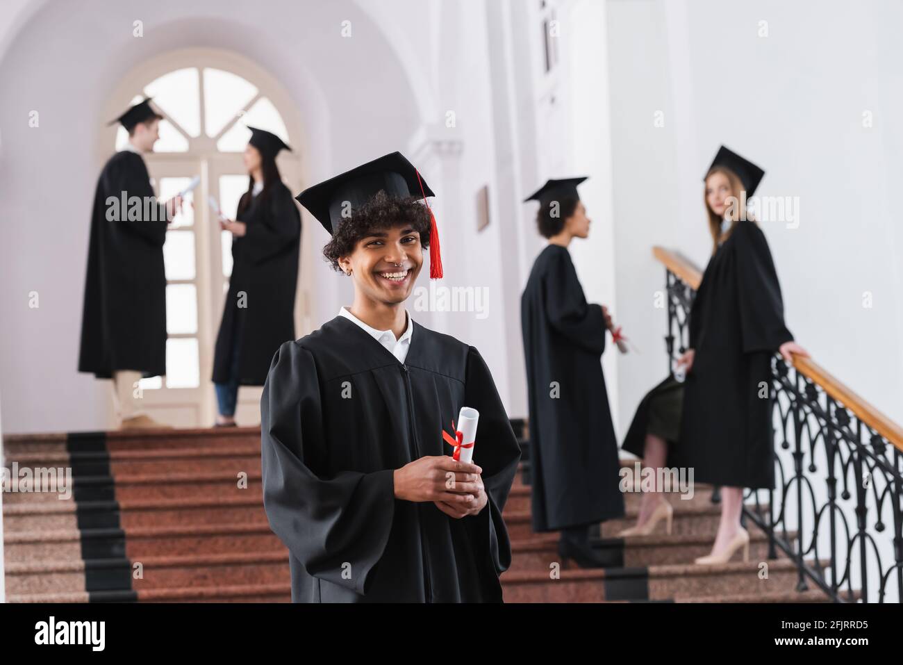 Giovane laureato afroamericano con un diploma che guarda la macchina fotografica dentro università Foto Stock