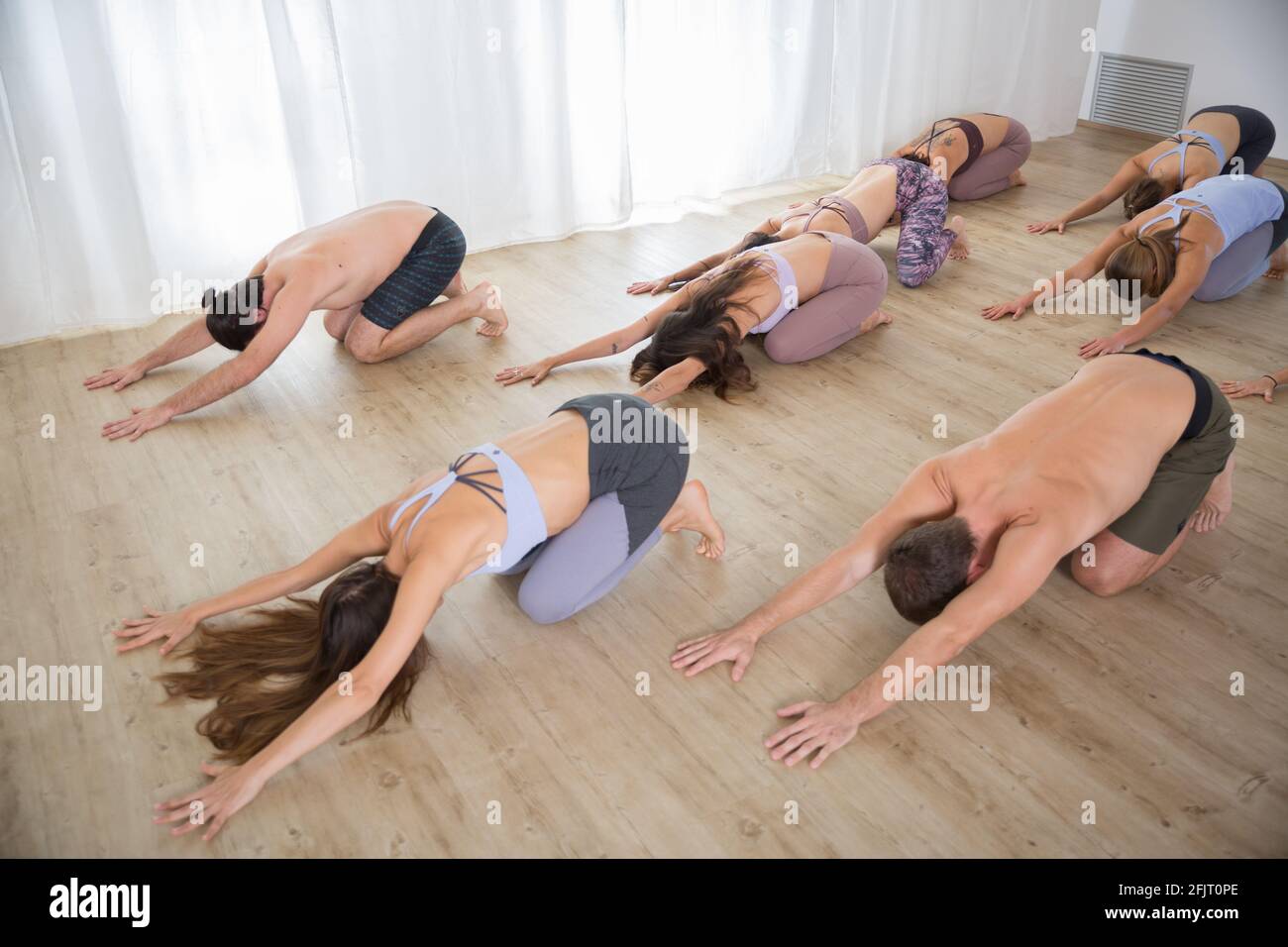 Gruppo di giovani sportivi attraenti in studio di yoga, lezioni di yoga con istruttore, in piedi, stretching e relax dopo l'allenamento Foto Stock