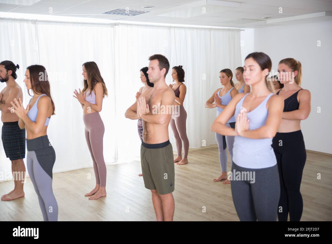 Gruppo di giovani sportivi attraenti in studio di yoga, lezioni di yoga con istruttore, in piedi, stretching e relax dopo l'allenamento Foto Stock