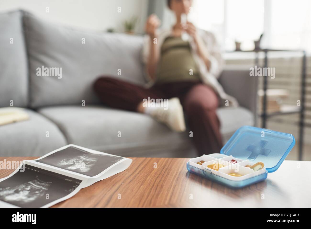 Primo piano di racconto con immagine ecografica con scatola con vitamine su di esso e donna incinta seduta sullo sfondo Foto Stock