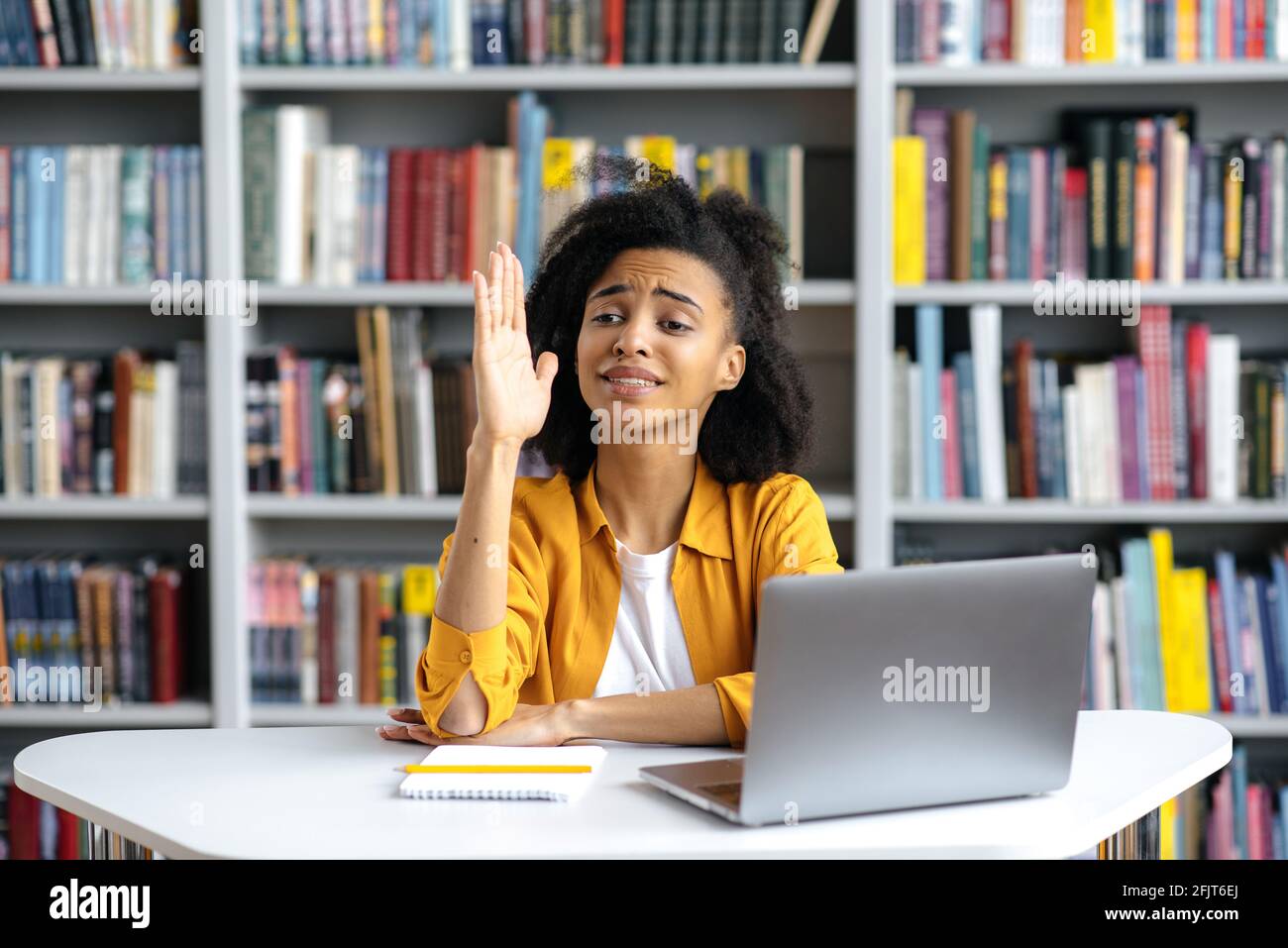 Intelligente sicuro bella studentessa di razza mista durante la lezione si siede al tavolo in abiti casual elegante, solleva la mano, conosce la risposta alla domanda e ha un'idea, vuole rispondere Foto Stock