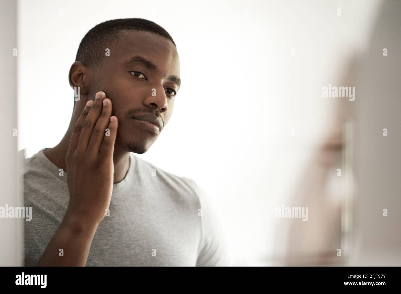 Uomo africano che esamina il suo volto in uno specchio da bagno Foto Stock