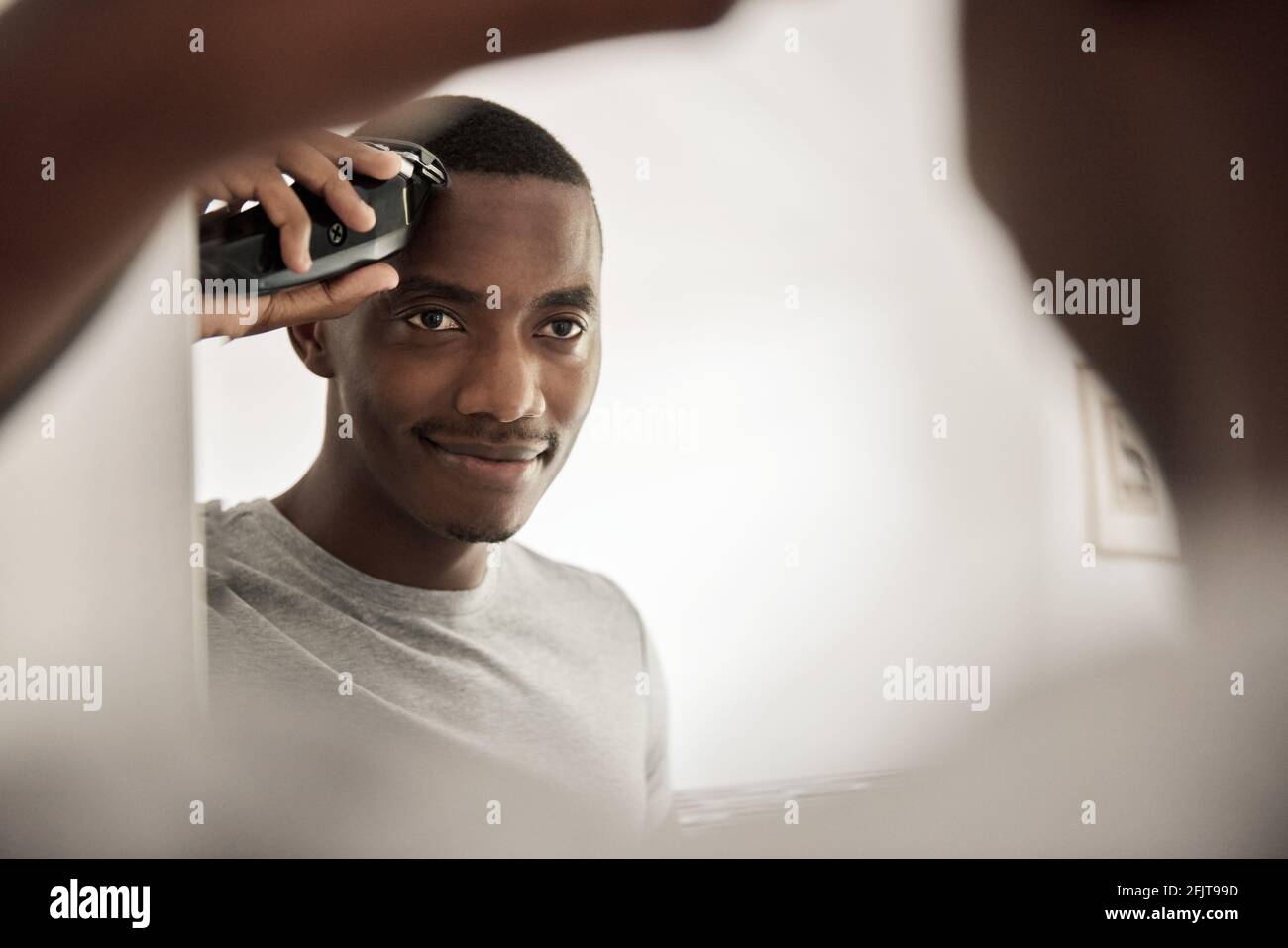 Sorridente uomo africano che taglia i capelli nello specchio del bagno Foto Stock