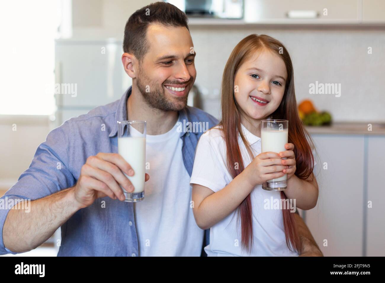 Papà felice e piccola figlia che beve latte seduto in cucina Foto Stock